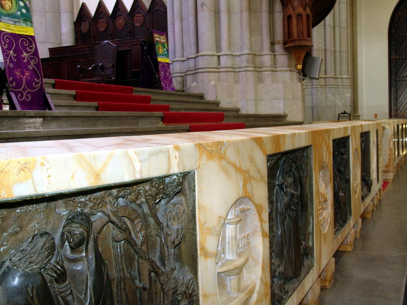 Pequeno muro de mrmore que circunda o altar, com placas metlicas encravadas, representando passagens bblicas